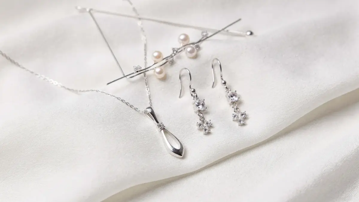 Brautschmuck neben weißem Brautkleid: Kette, Ohrringe und Haarschmuck passend zum Brautlook