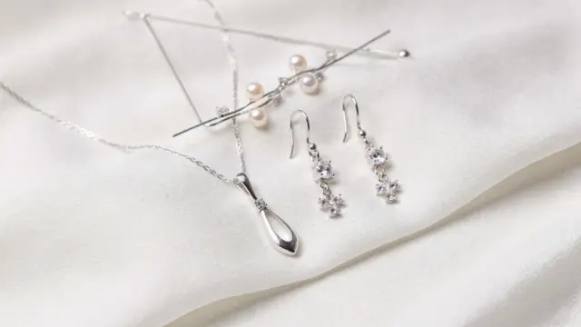 Brautschmuck neben weißem Brautkleid: Kette, Ohrringe und Haarschmuck passend zum Brautlook