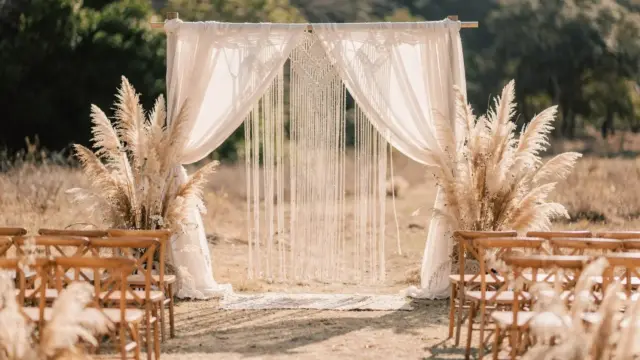 Boho-Hochzeit mit Makramee-Bogen, Pampasgras und Holzstühlen im natürlichen Outdoor-Setting